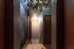 A narrow hallway with a wooden floor, a door at the end, and a hanging plant. - Deer Path Nara (Narashi Takamikadocho)