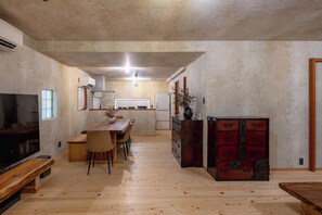 A spacious living area with a wooden dining table, chairs, a television, and a kitchen in the background. - Deer Path Nara (Narashi Takamikadocho)