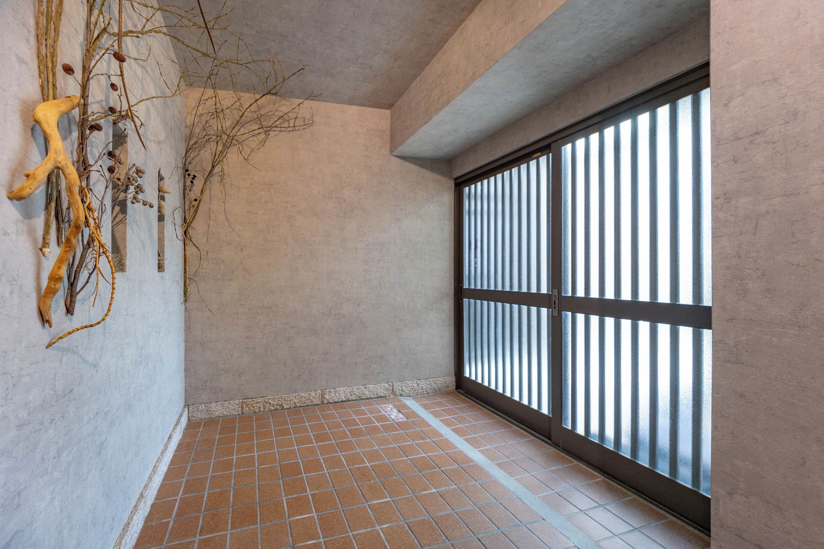 Una habitación con piso de baldosas, un ventanal con persianas verticales y ramas sujetas a la pared.