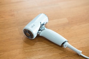 A hair dryer with a metallic base and a white handle on a wooden surface. - Deer Path Nara (Narashi Takamikadocho)