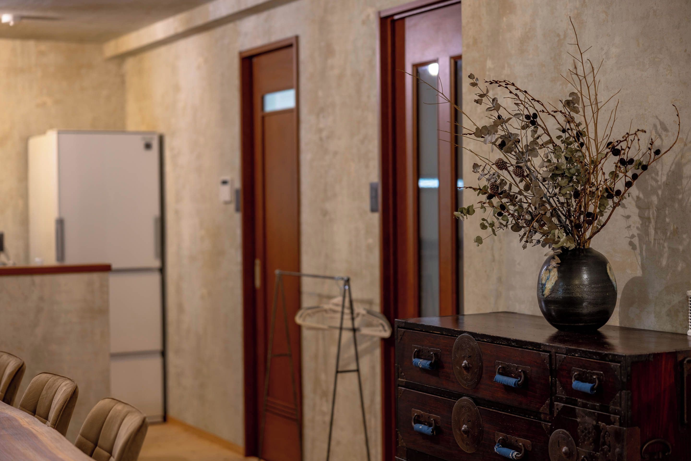 A room with a wooden cabinet, a vase with dried branches, and a white refrigerator.