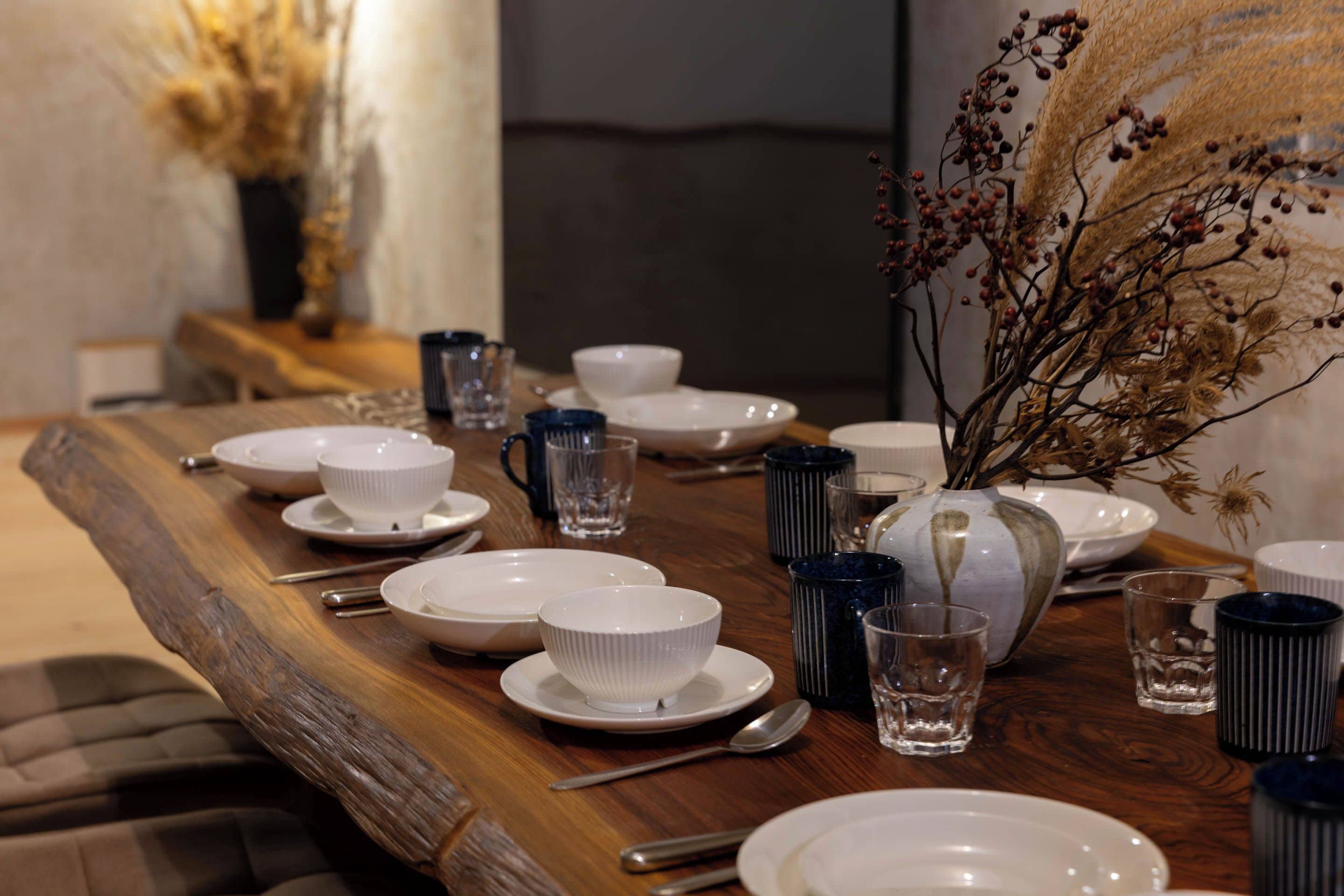 Una mesa de comedor dispuesta con platos blancos, tazones y tazas azules, junto con cubiertos y vasos transparentes.