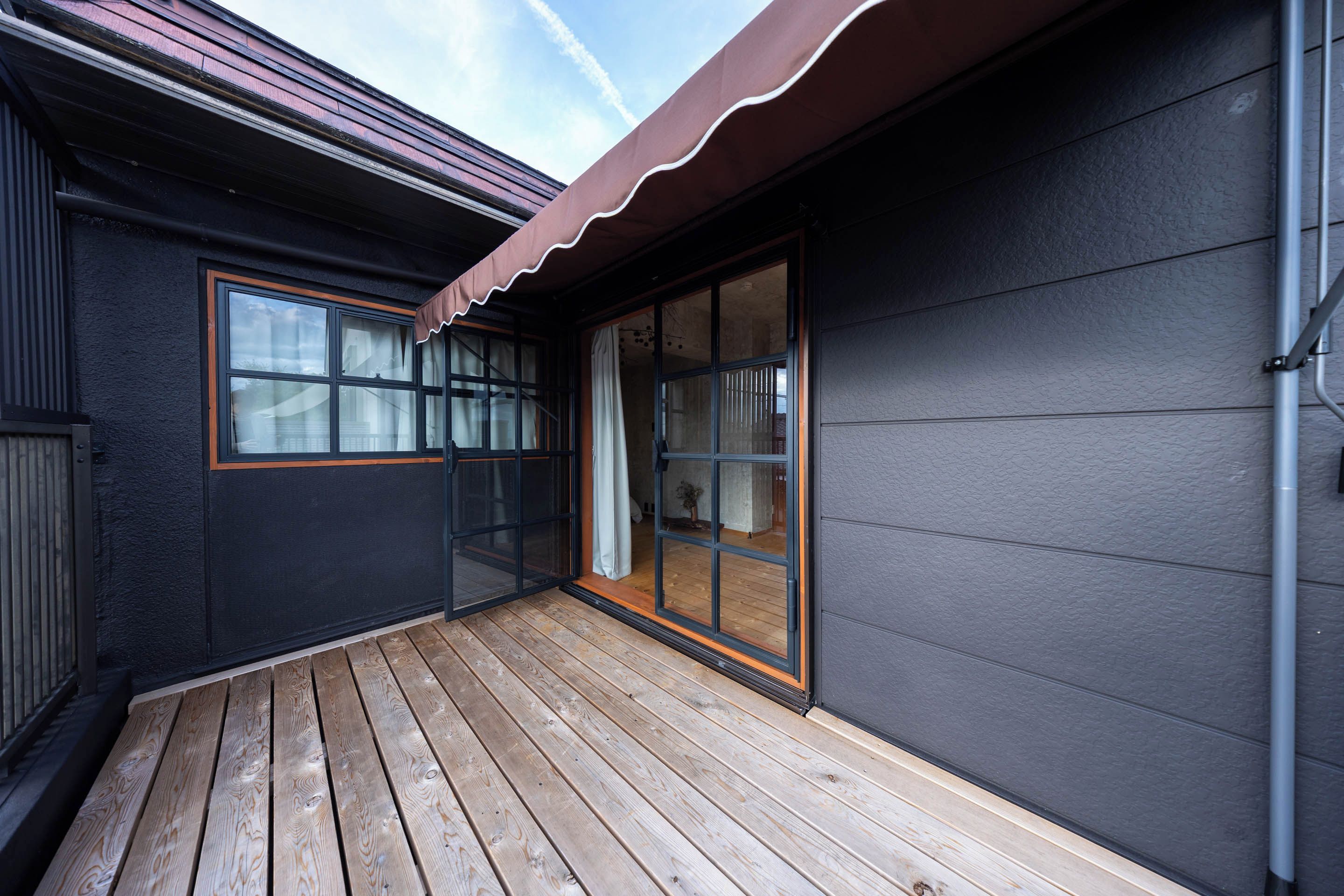 A wooden deck with a dark exterior wall and a sliding glass door leading to an interior space.