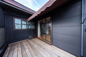 Une terrasse en bois avec un mur extérieur de couleur foncée et une porte-fenêtre coulissante donnant sur un espace intérieur.
