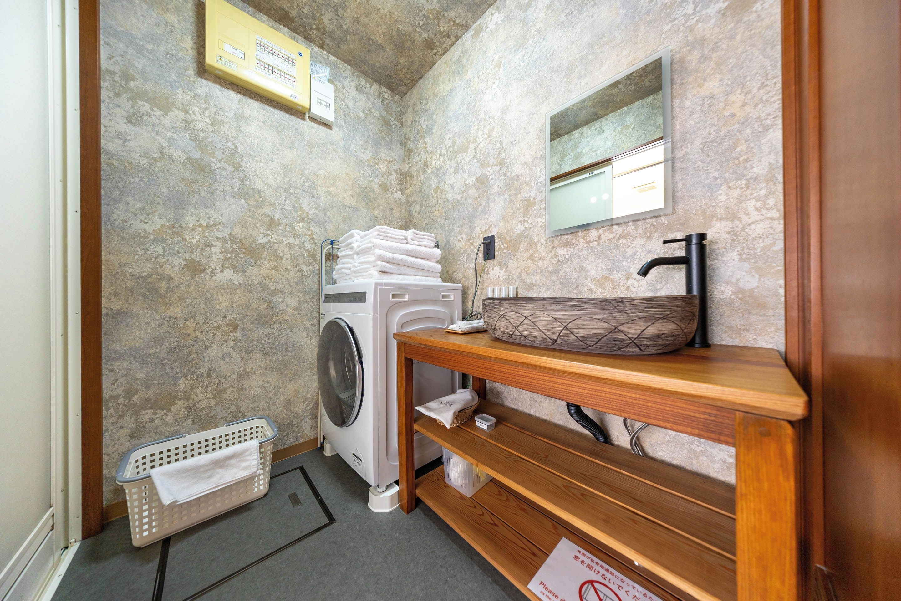A compact bathroom with a washing machine, a sink with a wooden countertop, and a mirror above it.