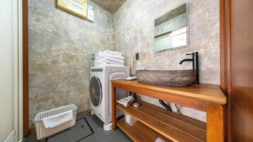 A compact bathroom with a washing machine, a sink with a wooden countertop, and a mirror above it.