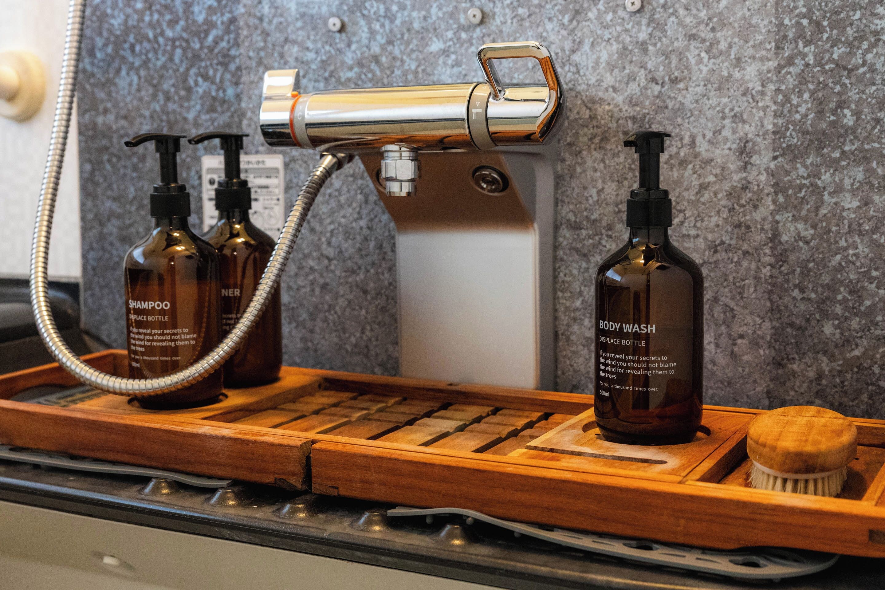 Une salle de bain avec un plateau en bois contenant des flacons de shampoing et un flacon de gel douche, une pomme de douche et une brosse en bois.