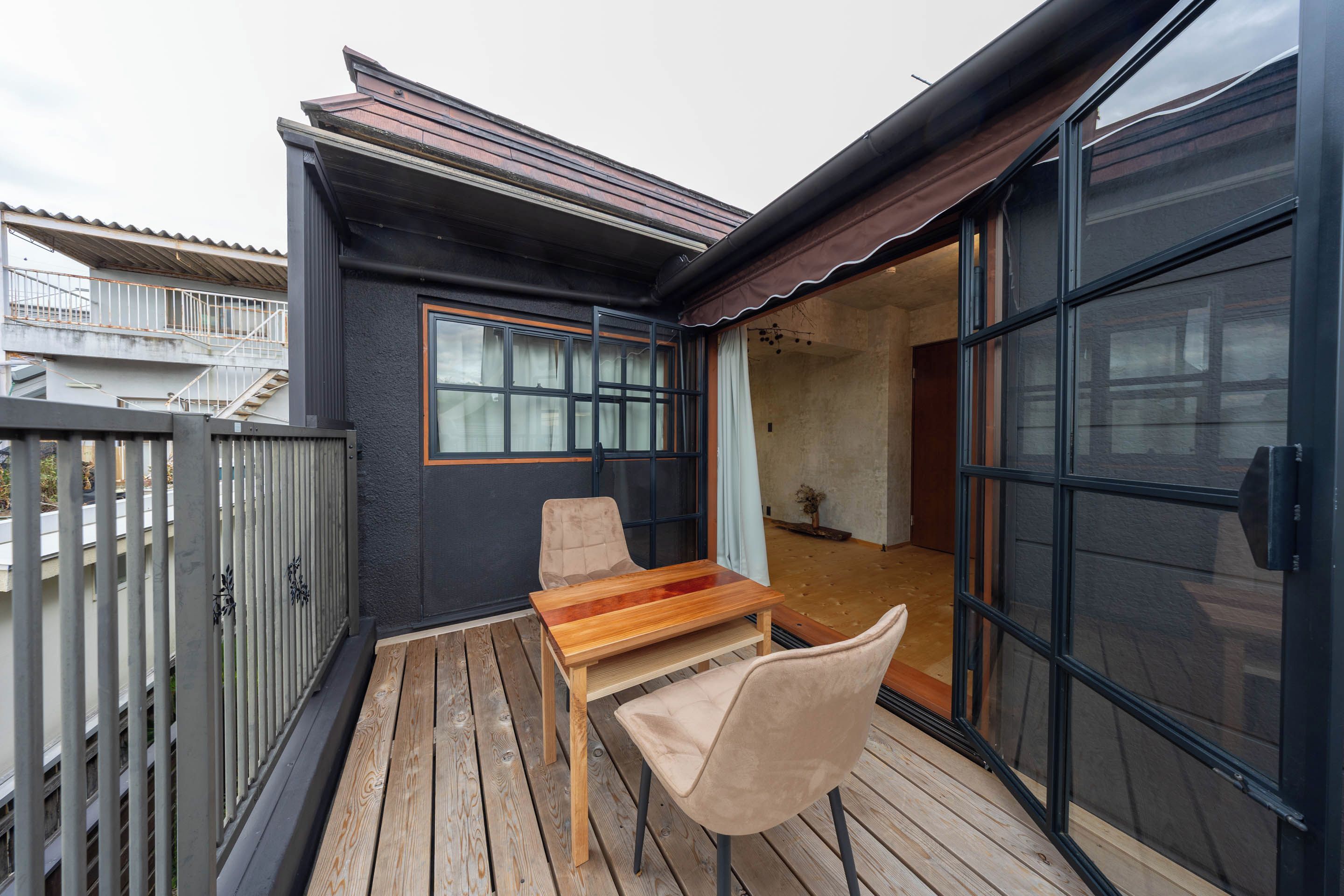 A balcony with a wooden table and two chairs, a sliding glass door, and a view of the street.