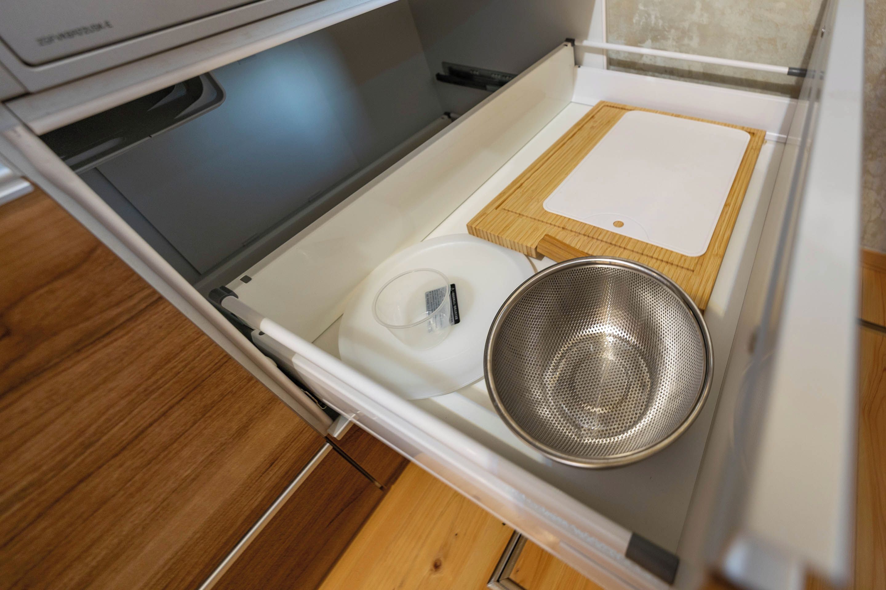A kitchen drawer with a white appliance, a metal strainer, and a wooden cutting board.