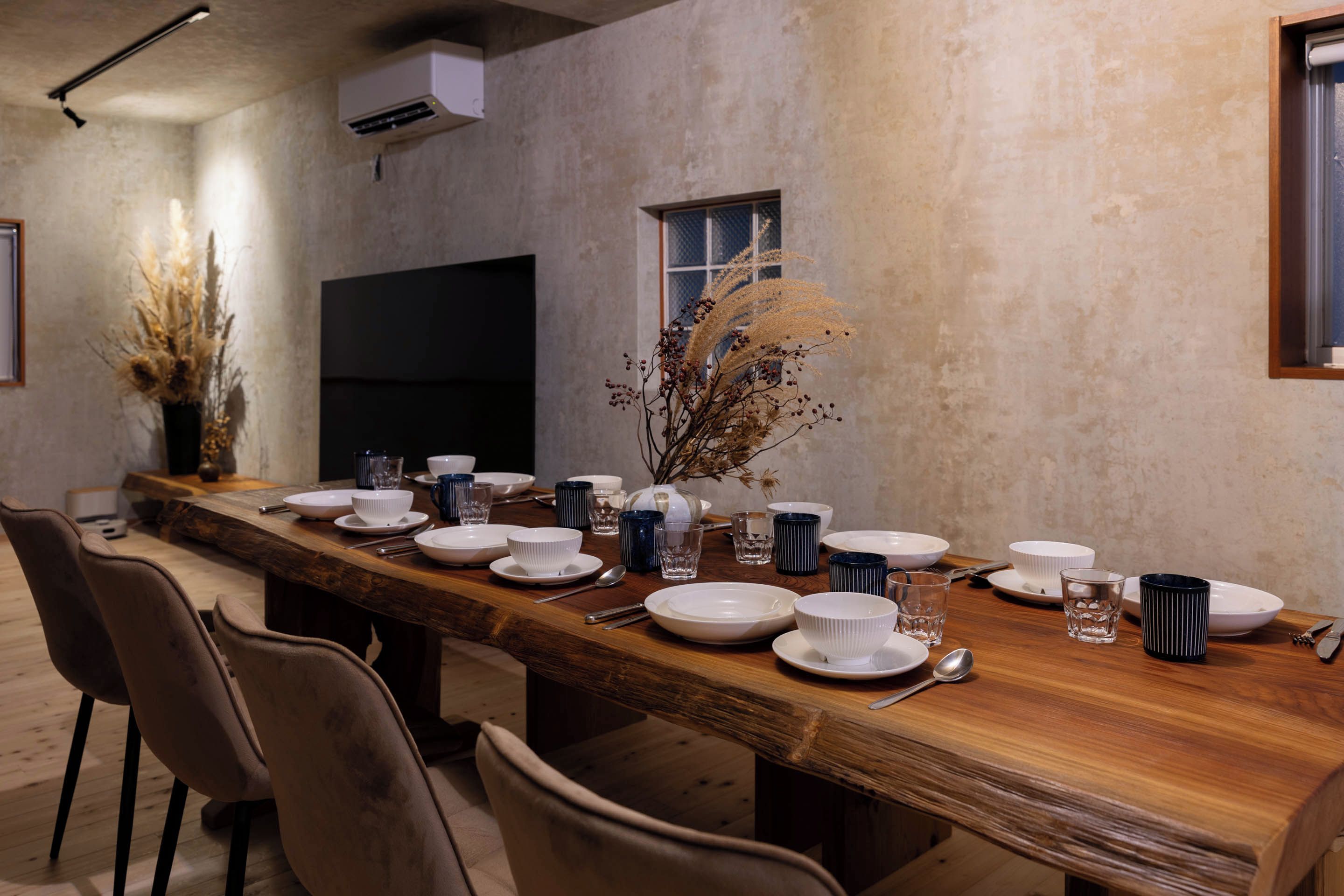 A long dining table set with white plates, bowls, and glasses, flanked by chairs.