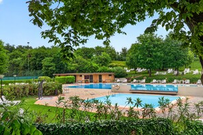 Ein Swimmingpool mit Liegestühlen, ein kleines Gebäude und üppiges Grün.