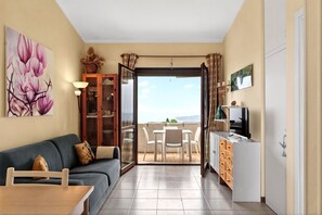 Une pièce comprenant un canapé, une table à manger, un coin cuisine et une porte-fenêtre coulissante donnant sur une terrasse extérieure.