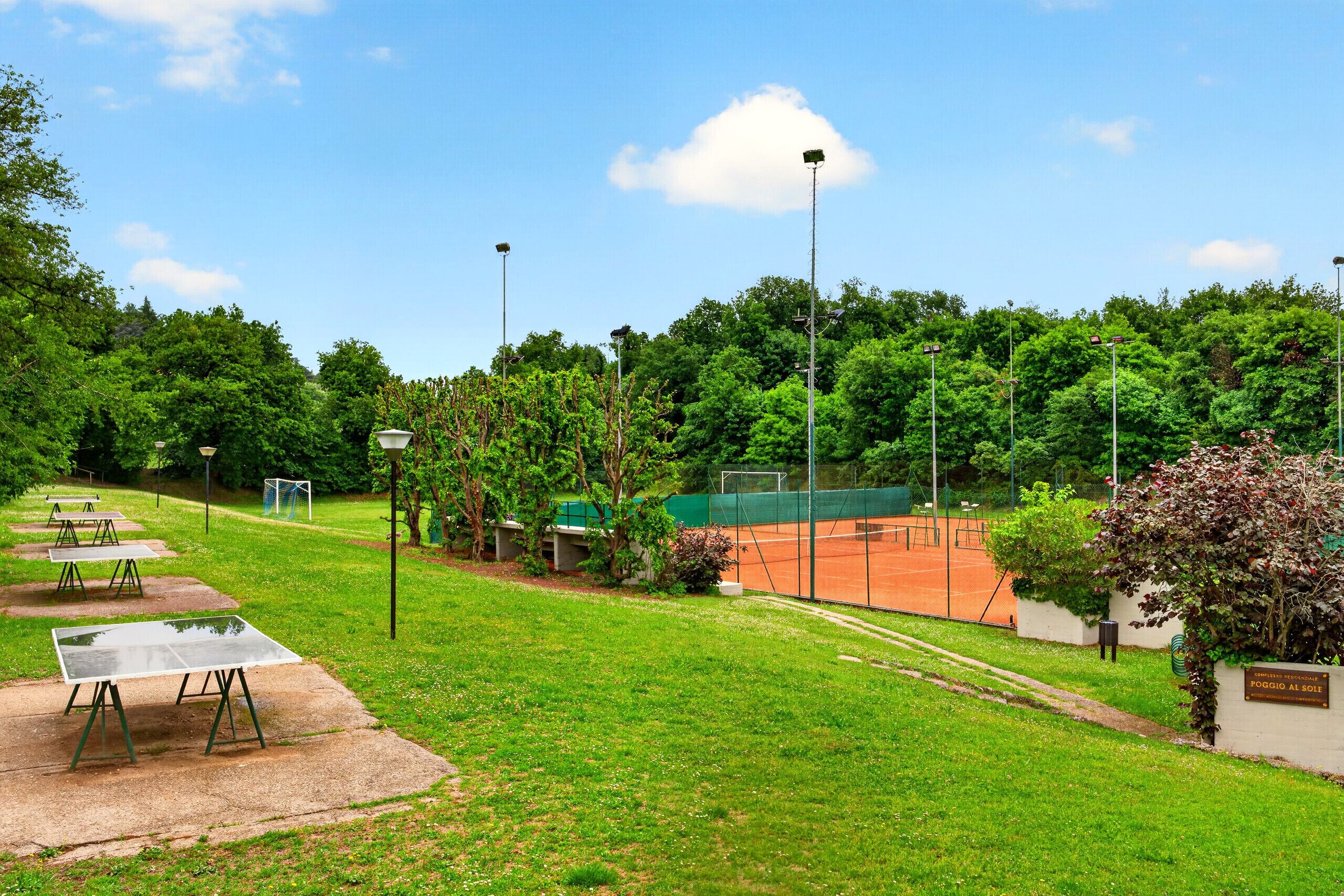 A tennis court with a net, surrounded by trees and a clear sky.