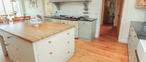 Uma cozinha com piso de madeira, armários brancos, uma ilha central e fogão embutido.