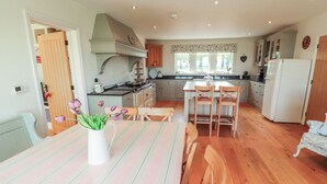 A kitchen with wooden flooring, a dining table with striped tablecloths, and a white vase with flowers. - Thimble Hill (Carlisle)
