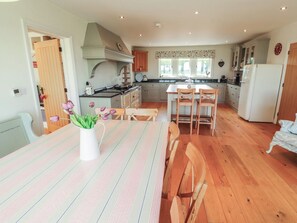 A kitchen with wooden flooring, a dining table with striped tablecloths, and a white vase with flowers. - Thimble Hill (Carlisle)