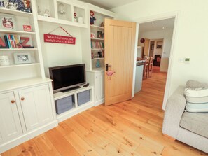 A living room with a television, shelves with books and decorations, a wooden door, and a sofa. - Thimble Hill (Carlisle)