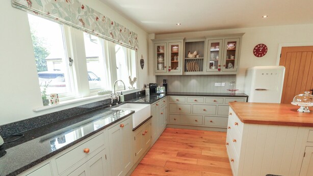 A kitchen with wooden flooring, white cabinets, a granite countertop, and a window with a floral curtain. - Thimble Hill (Carlisle)