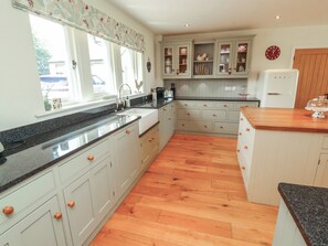 A kitchen with wooden flooring, white cabinets, a granite countertop, and a window with a floral curtain. - Thimble Hill (Carlisle)