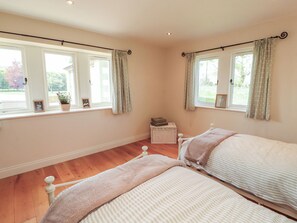 A bedroom with two beds, a window with curtains, a small table, and a potted plant. - Thimble Hill (Carlisle)