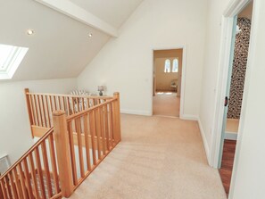 A spacious loft bedroom with a sloped ceiling, a wooden staircase, and a view of a bedroom through a door. - Thimble Hill (Carlisle)