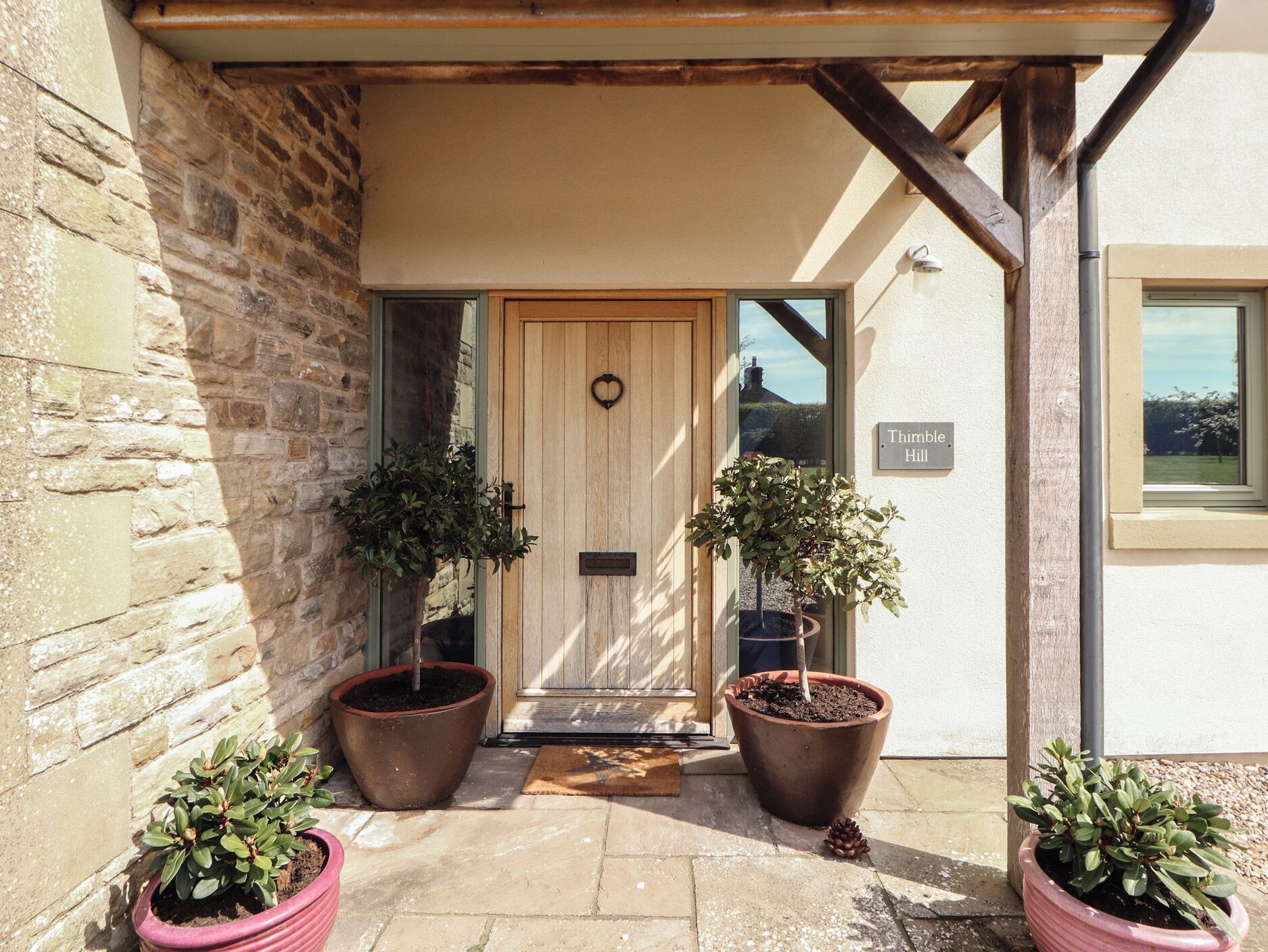 A stone building with a wooden door, two potted plants, and a sign reading 'Thimble Hill'.