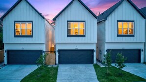A row of three modern houses with garage doors, each with a number displayed above the door.