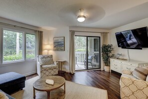 A living room with a sofa, armchair, coffee table, TV, and a sliding glass door leading to a balcony. - Sunset Rentals | Colonnade Club 147 (Hilton Head Island)