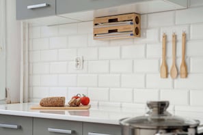 A kitchen with white tiled backsplash, wooden cutting board with bread and tomatoes, and wooden utensils hanging on the wall. - Bright Apartment | Remote Working | Planetarium (Toruń)