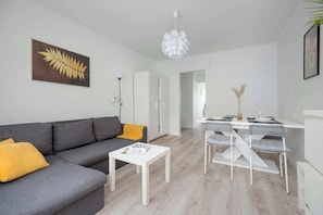 Un salon moderne avec un canapé gris, une table basse blanche et un coin repas comprenant des chaises et une table blanches.