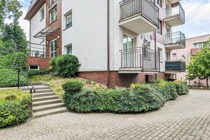 Un edificio residencial de varios pisos con fachada de ladrillo, una escalera central y un pequeño jardín con setos.