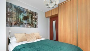 Un dormitorio con una cama, un edredón verde acolchado, un armario de madera y una obra de arte en la pared.