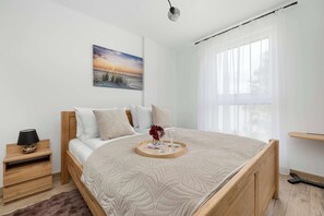 A bedroom with a bed, bedside table, nightstand, and a window with curtains. - Cosy Apartment in a Modern Development | Balcony & Parking (Mielno)