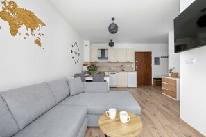 A modern living room with a grey sectional sofa, a wooden coffee table, and a flat-screen TV mounted on the wall. - Cosy Apartment in a Modern Development | Balcony & Parking (Mielno)