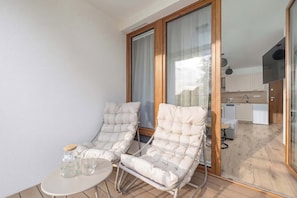 Un balcone con due poltrone imbottite, un tavolino e un vasetto di vetro.