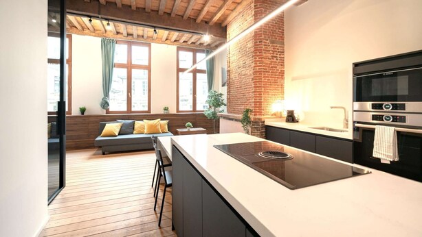 A modern kitchen with a large island, a built-in oven, and a dining area with a sofa and chairs. - Apartment for 6 With Antwerp City Views (Antwerp)