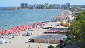 A beach with umbrellas, a lifeguard tower, and a building with a flat roof. - Vila Naty (Mamaia-Sat)