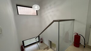 A staircase with a glass handrail, a fire extinguisher, and a pendant light. - Vila Naty (Mamaia-Sat)