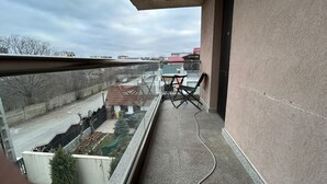 A balcony with a table and chairs, a view of a street, and a building in the background. - Vila Naty (Mamaia-Sat)