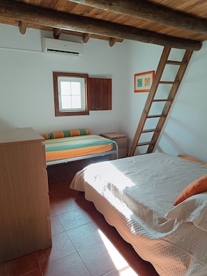 A bedroom with a bunk bed, a window, a wooden ladder, and a framed picture on the wall.