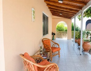 A covered patio area with wicker furniture, a window, and potted plants.