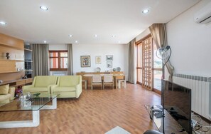 Un saló espaiós amb un sofà, una taula de café de vidre, una zona de menjador amb taula i cadirees, i una finestra gran amb cortines.