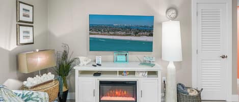 Una sala de estar con chimenea, televisor, un reloj y cuadros en la pared.