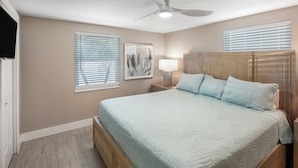 A bedroom with a bed, a nightstand, a lamp, a ceiling fan, and two windows with blinds.
