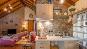 A cozy kitchen with a stone wall, wooden cabinets, a built-in oven, and a window with decorative glass. - Rural Cabin 'La Casita de la Font del Bosc'. SPA. Charming Entire Rural House (La Font del Bosc)