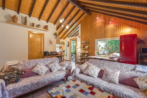 A cozy living room with a wooden ceiling, two patterned sofas, a tiled coffee table, and a red appliance.