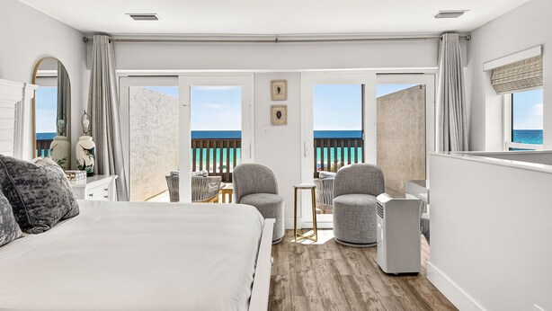 A hotel room with a bed, a seating area with chairs, a small table, and a view of the sea. - beachfront townhome located directly on the sand in a private gated community (Panama City Beach)