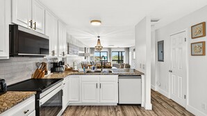 A modern kitchen with white cabinetry, granite countertops, a black stove, and a large window. - beachfront townhome located directly on the sand in a private gated community (Panama City Beach)