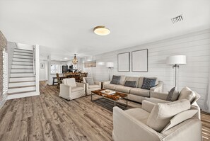 Ein geräumiger Wohnbereich mit Holzboden, einer Sofagarnitur, einem Couchtisch und einer Treppe zu einem anderen Raum.