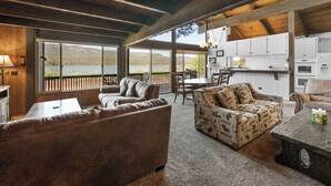 Amplia sala de estar con un gran ventanal con vista a un lago, amueblada con sofás y una mesa de comedor.